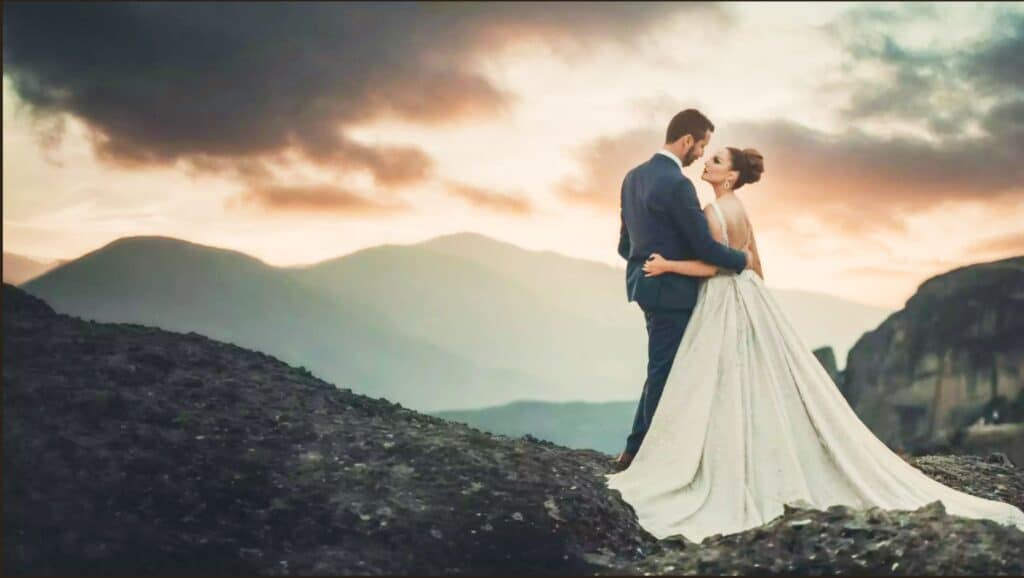 A bride and groom are standing in front of a breathtaking backdrop of towering mountains under a dynamic sky. The bride wears a flowing white dress, and the groom is dressed in a sharp suit. The marriage preparations they made will help them to have a lifelong marriage.