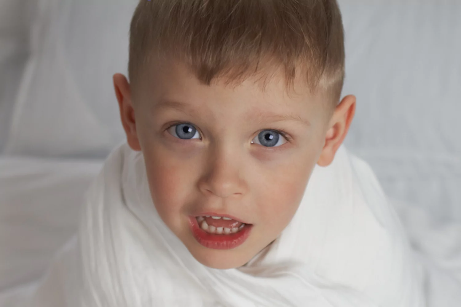 four year old boy with big blue eyes wrapped in his bedsheet as he explains his bed-wetting accident