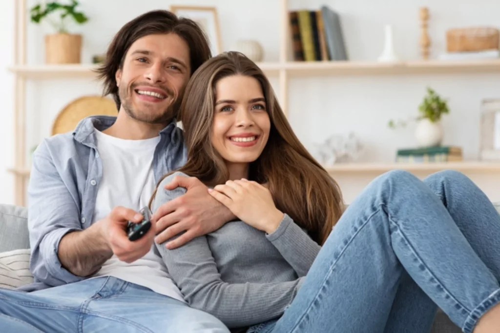 A couple sits together on a cozy couch, watching tv. They believe couples should live together before marriage.