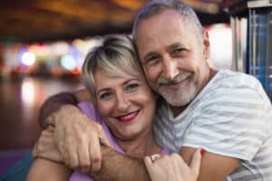 A joyful middle-aged couple hugging and smiling warmly at the camera, representing a strong and happy marriage. They have learned how to not let past relationship affect their marraige.