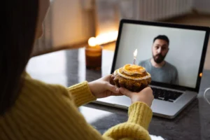 A woman holds a cupcake with a lit candle while video chatting with her husband, symbolizing the challenges and intimacy of a long-distance marriage.