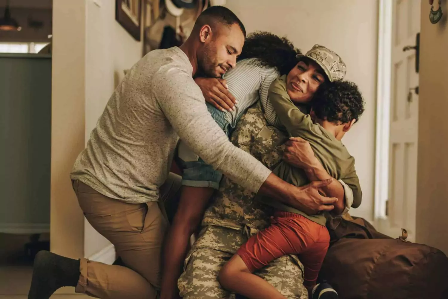 A military service member in uniform embraces her family, who are all gathered tightly around her, representing the emotional reunion after a deployment.