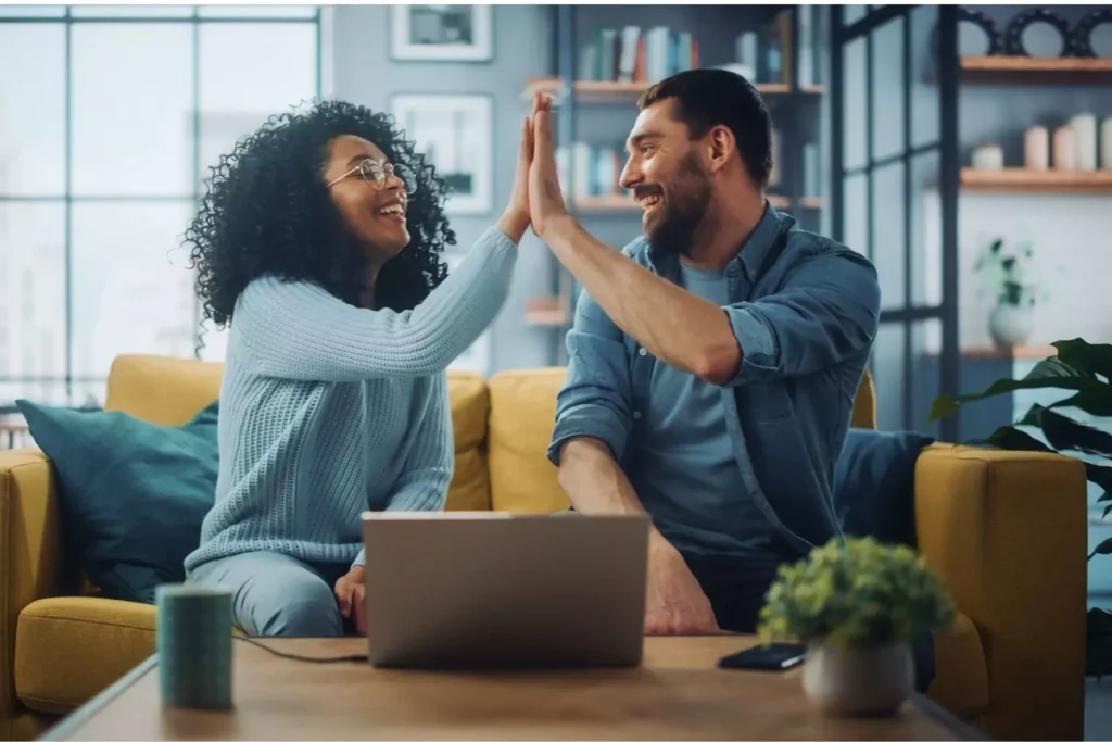 A couple celebrating how they have made it a goal in their marriage to make every situation a win-win situation by giving each other a high five on the couch.