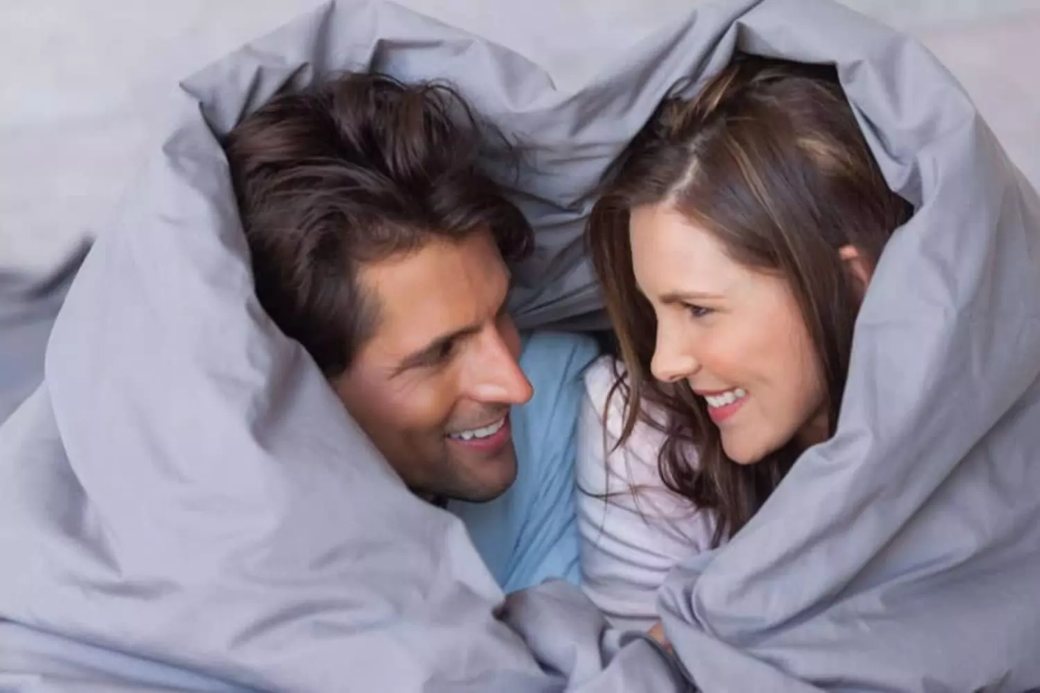 A husband and wife are wrapped up in a blanket, that creates a heart shape around them, symbolizing the sexual intimacy that helps to create a healthy marriage.