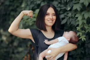 A fierce woman holding a baby in one arm while flexing her other arm in a display of strength and confidence as God's created daughter.