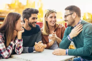 Four friends, two married couples, sit together at an outdoor table, sharing laughter and engaging in meaningful conversation, symbolizing the value of investing in other married couples.