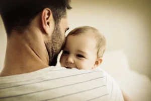 Father holding and embracing his smiling baby, symbolizing the love and care of God the Father.