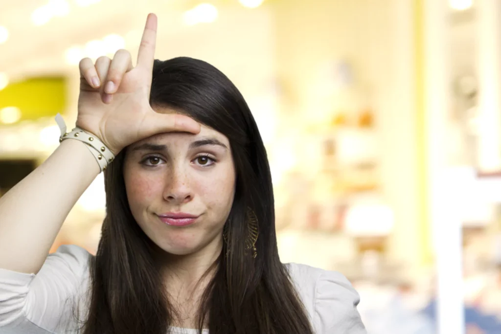 Mean girl holding her hand to her forehead in the L shape for loser