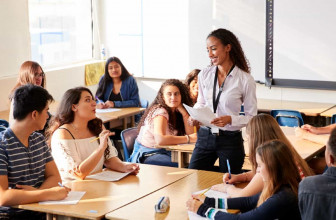 Young, smiling female teacher standing among her high school students in classroom