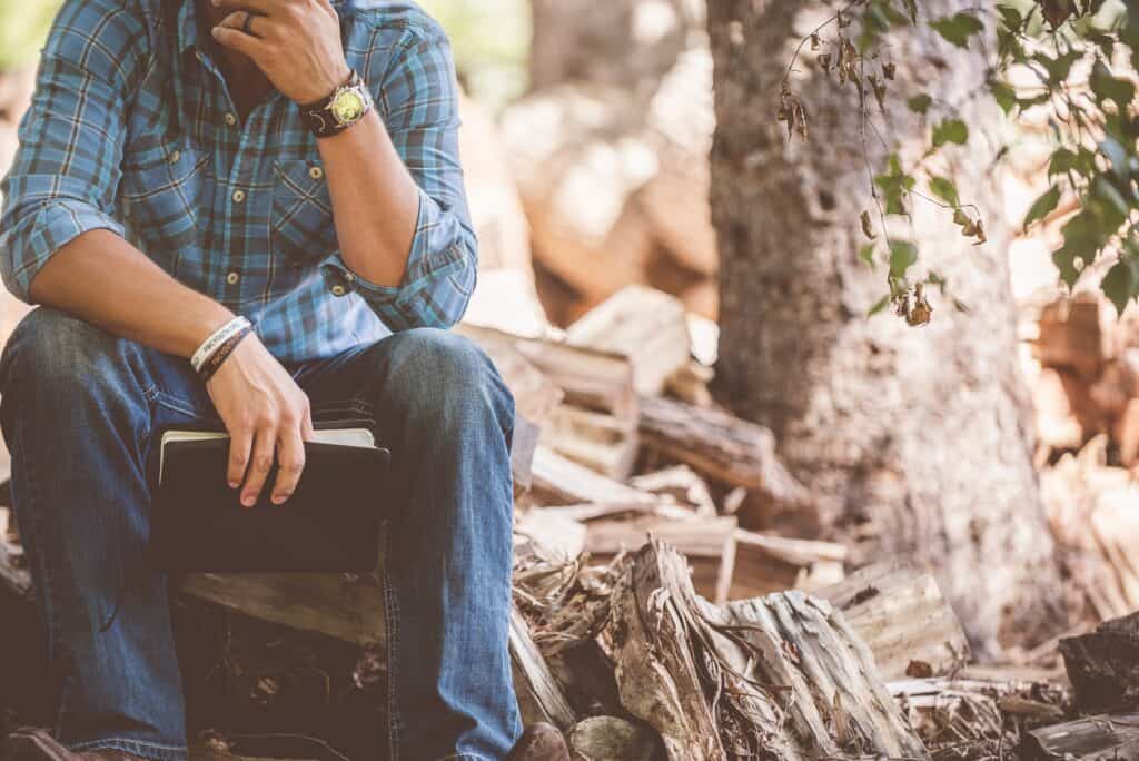 man holding Bible sitting in the woods