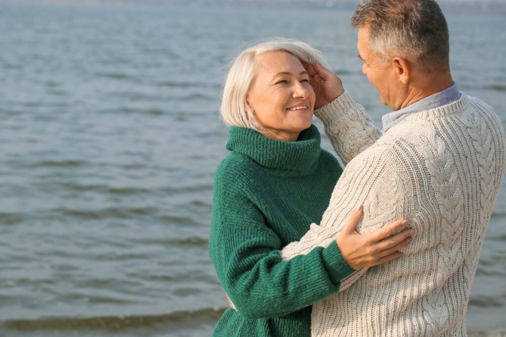 Older man and woman embracing by ocean