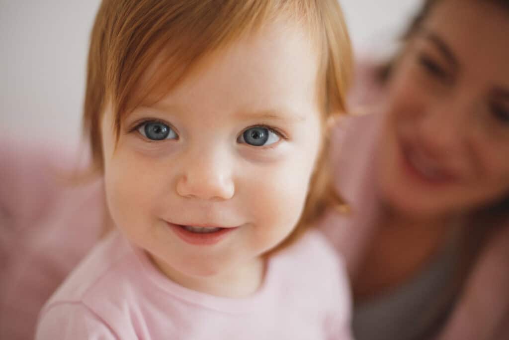 toddler girl smiling, mom in background