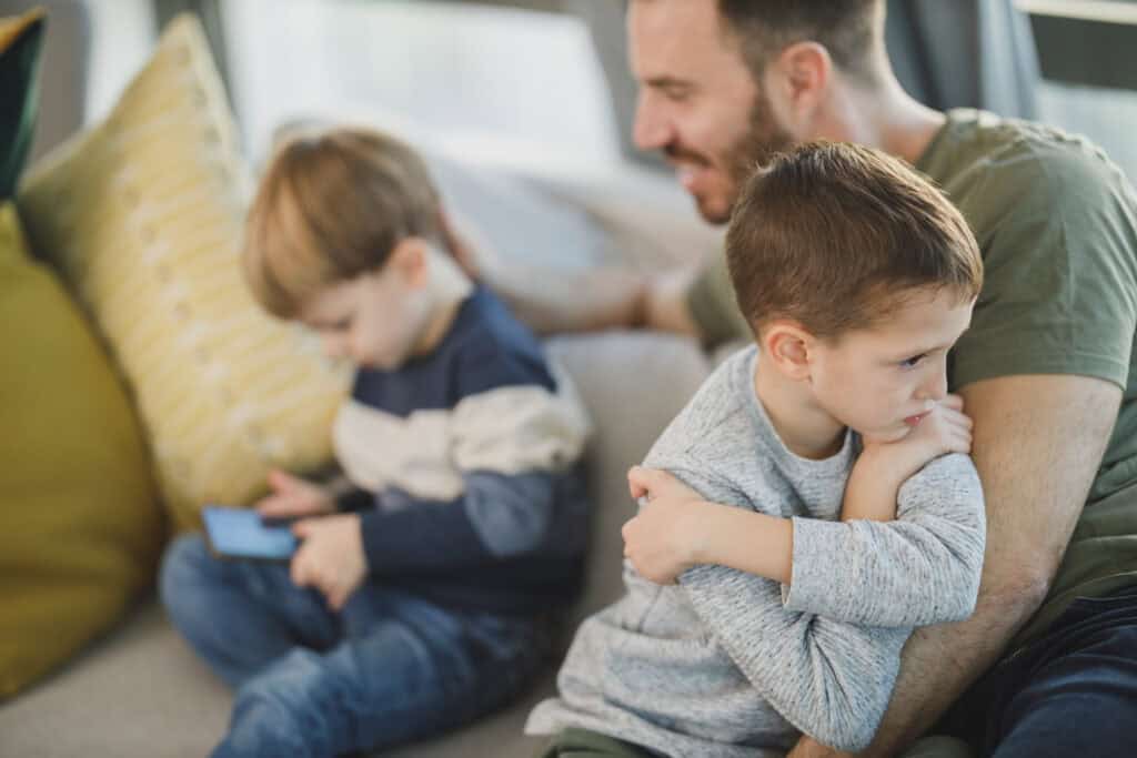 angry boy in dad's lap near sibling