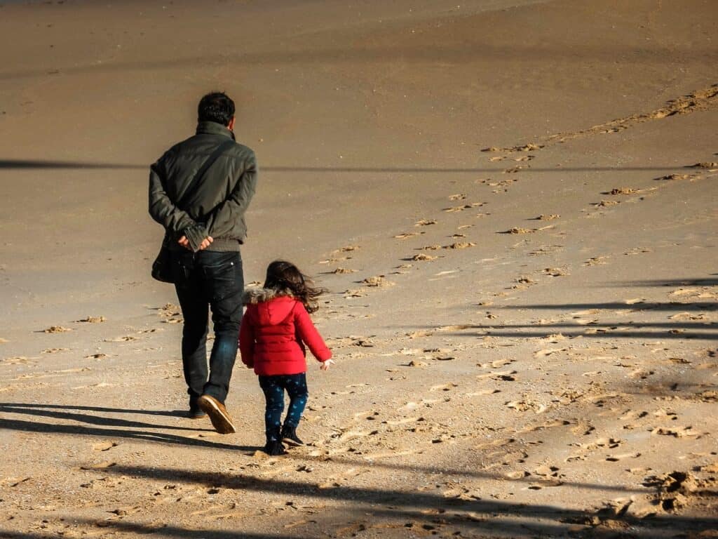 Dad and little girl walking on beach