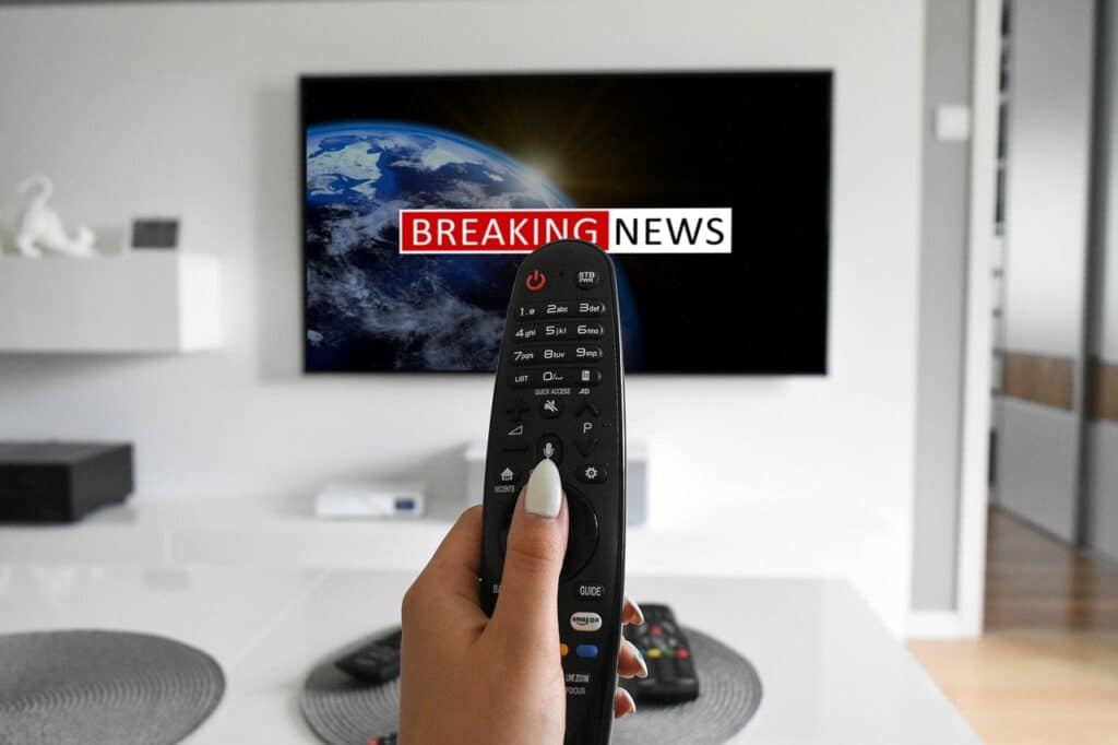 Picture of woman holding a remote control toward TV screen that reads Breaking News