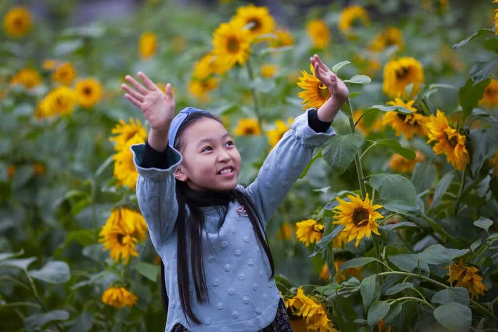 girl in sunflower field lifting hands smiling