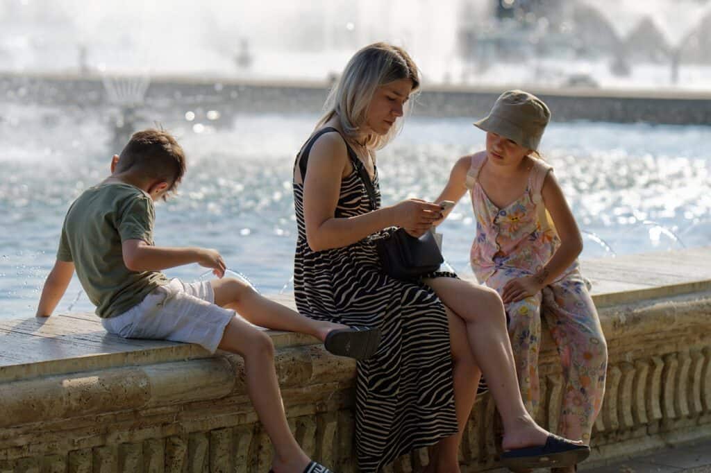 mom and two kids sitting by fountain