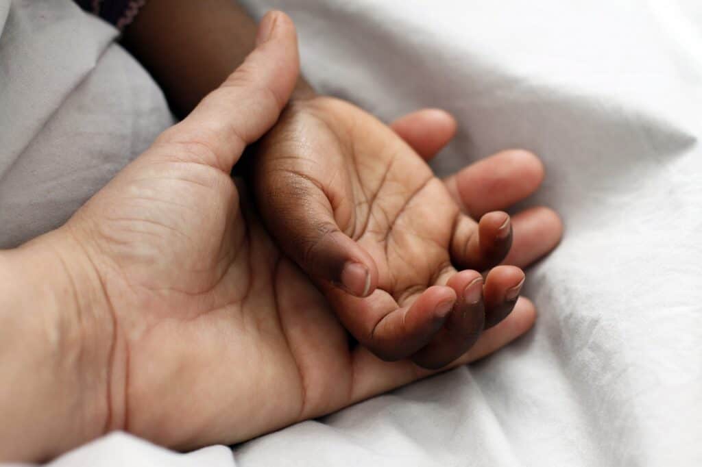 Light skinned adult hand holding darker child hand