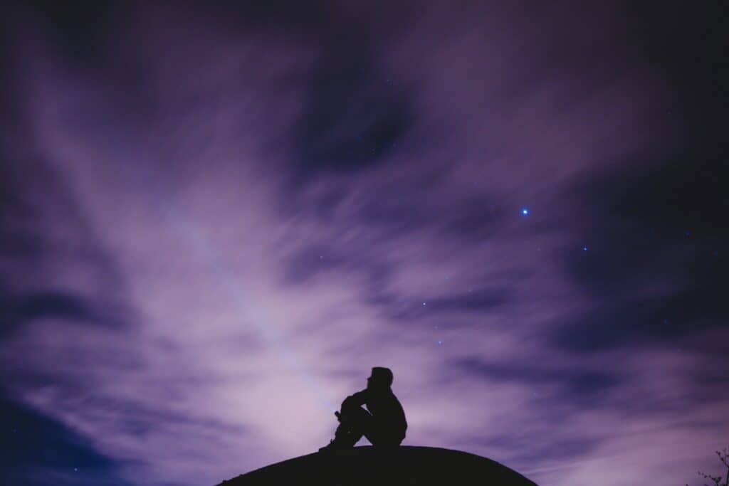 shadow of person sitting under mysterious purple sky
