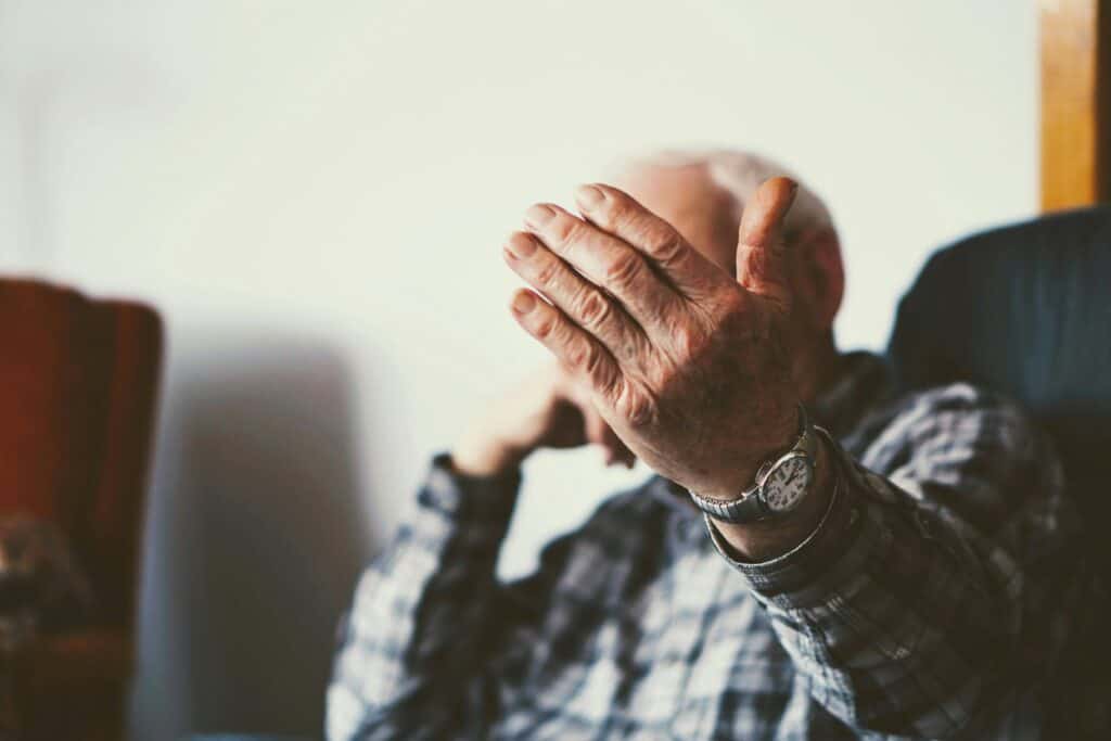 old man sitting beckoning with hand or covering face