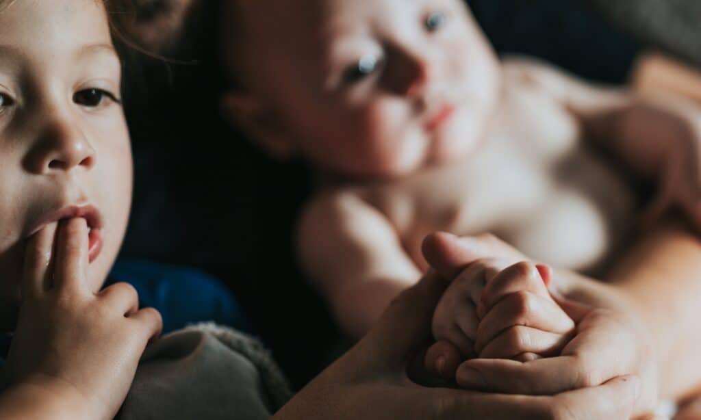 Child sucking on fingers baby in background