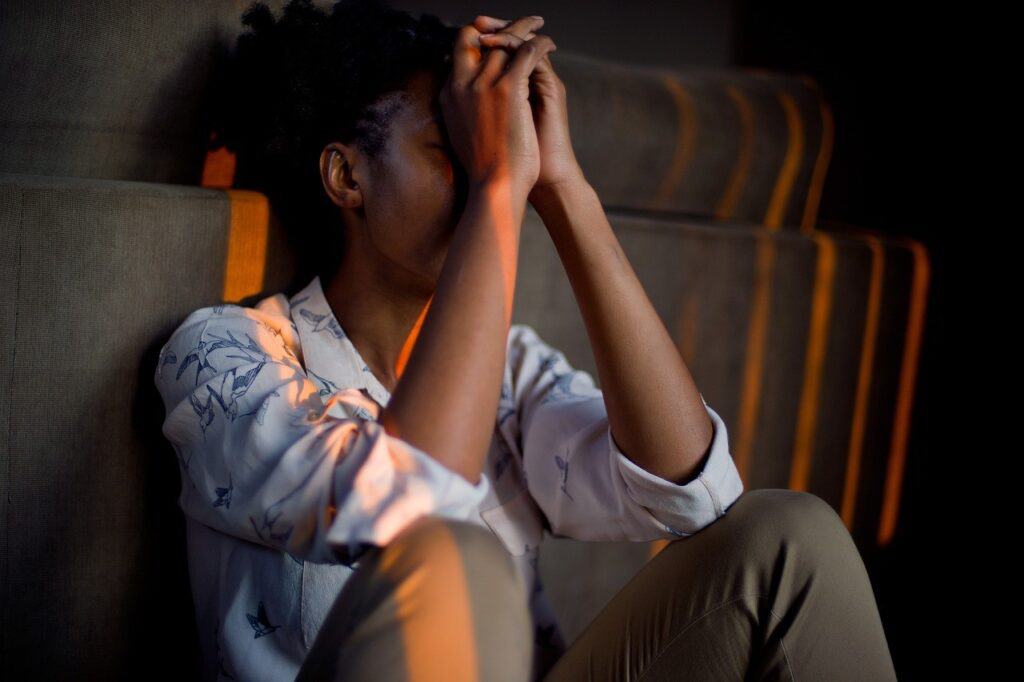 girl sitting in shadow elbows on knees sad