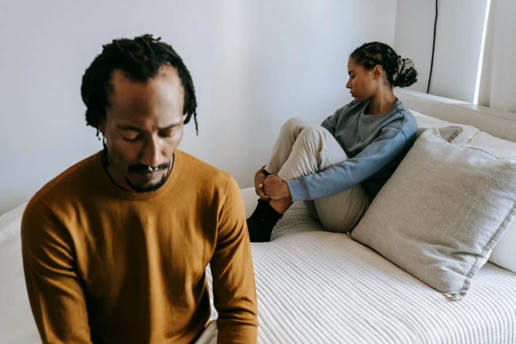 man and woman sitting on bed looking away from each other