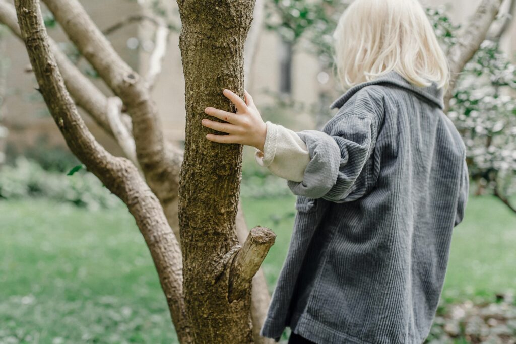 back of child standing beside a tree