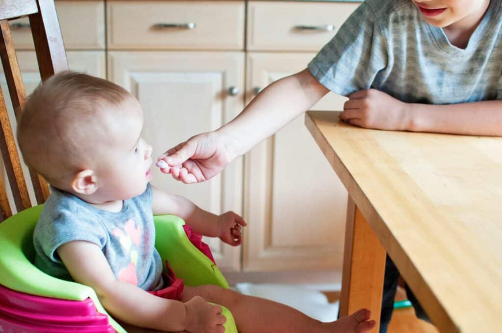 young boy feeding snack to baby at table