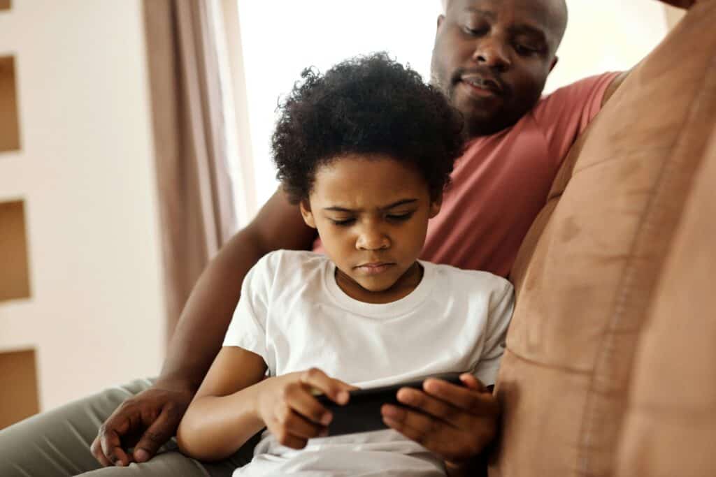 boy sitting on dad's lap with phone scowling