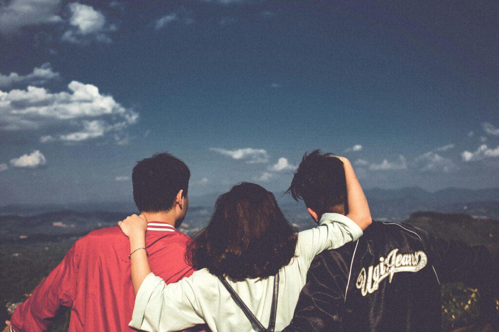 two guys with girl in the middle arms around both looking out over mountain