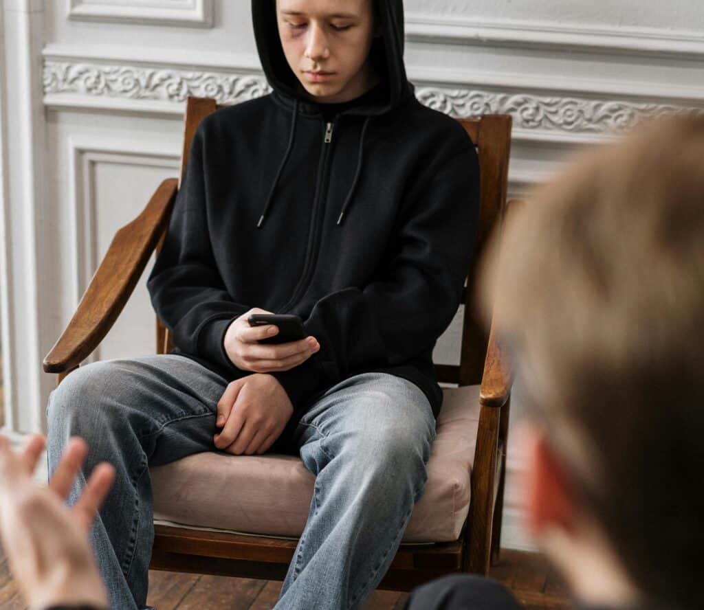 Teen boy in hoodie looking at phone while man in foreground tries talking to him