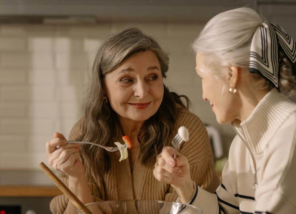 two older women smiling eating salad out of bowl