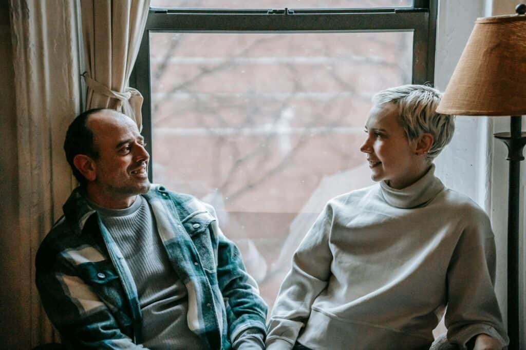 40s couple looking at each other in front of window