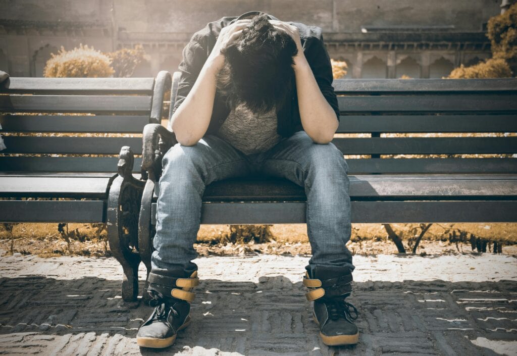 boy leaning over on bench head in hands