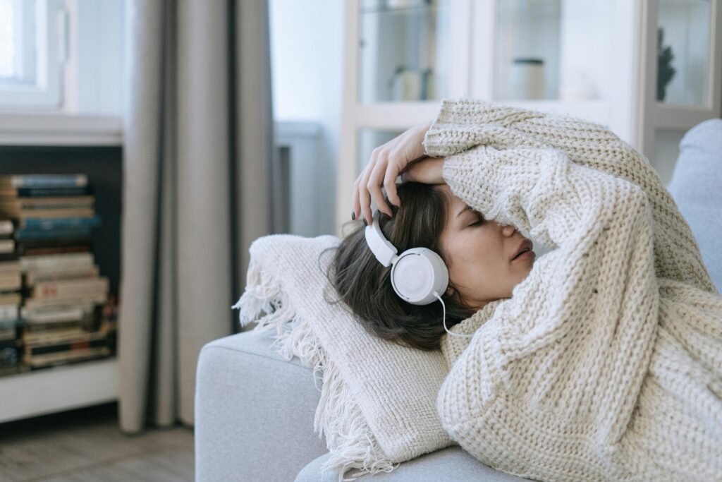 woman lying on couch headphones hands on head sad