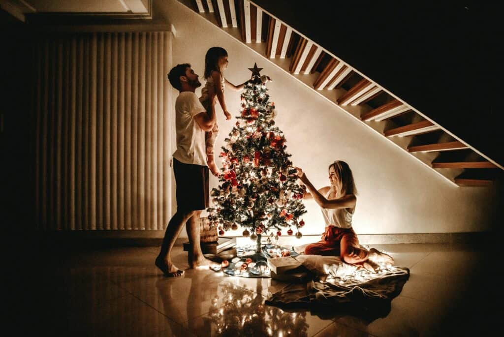 mom dad and child lighting small Christmas tree