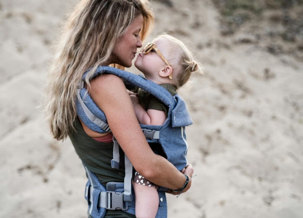 mom holding little girl in carrier kiss