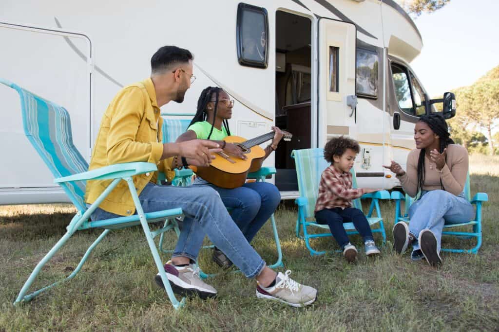family sitting outside of RV playing guitar