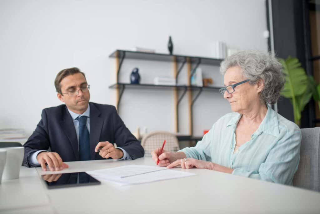 older woman signing papers with man in suit