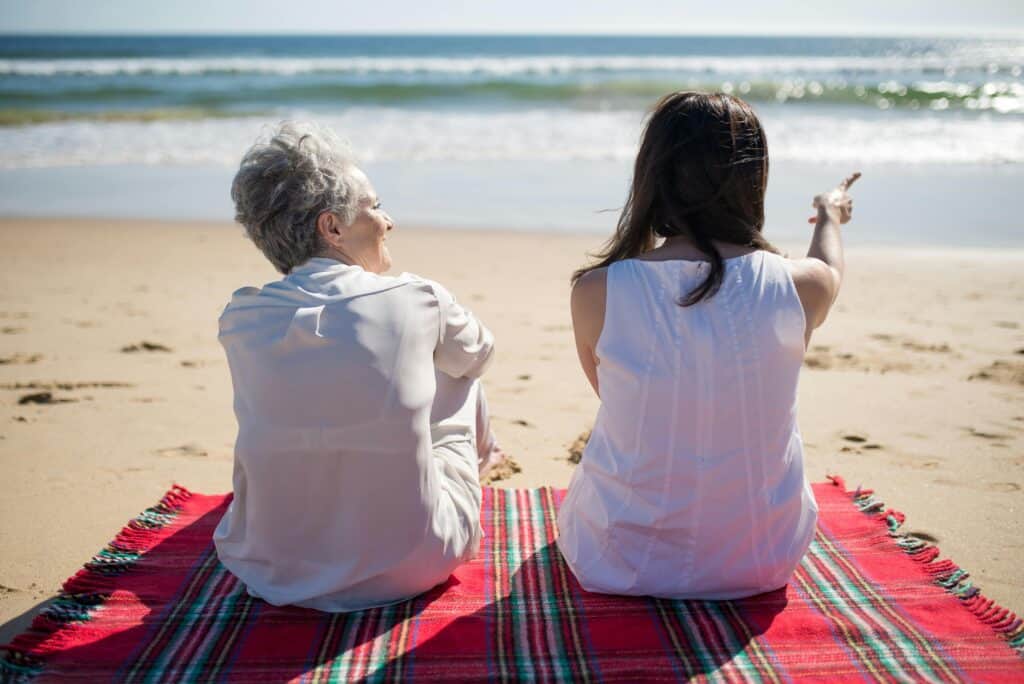 mom and adult daughter on blanket on beach