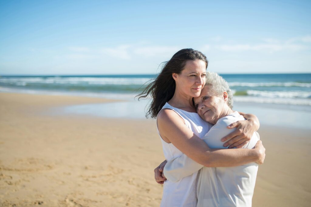 older mom and daughter hugging on beach