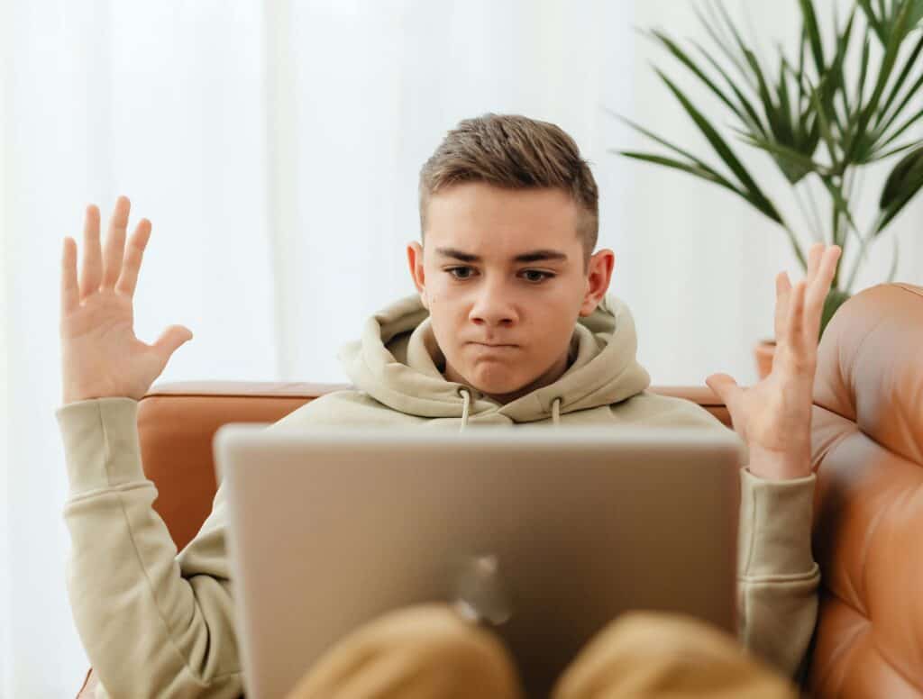 teen lifting arms angrily while looking at laptop