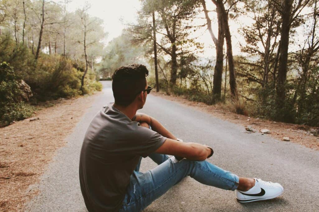 teen guy sitting on forest road pondering