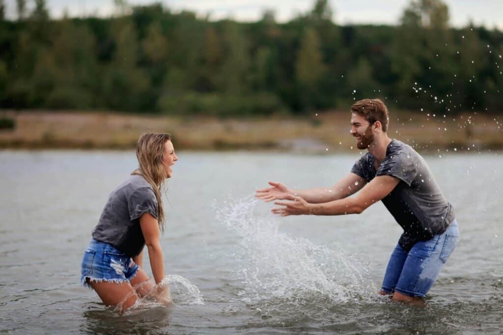 man and woman in lake splashing each other couple fun