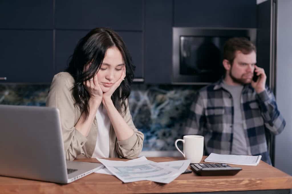 Wife sitting by computer with bills and calculator man on phone