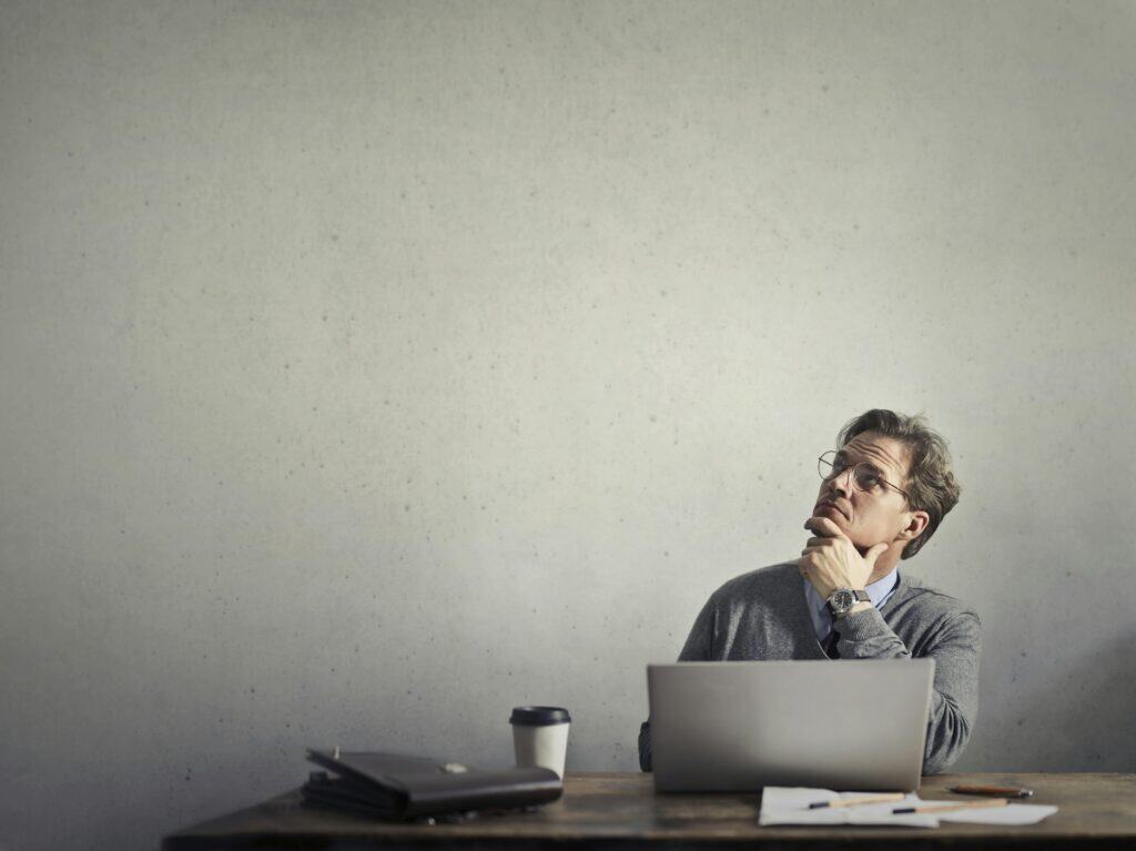 Man on computer pondering looking in air