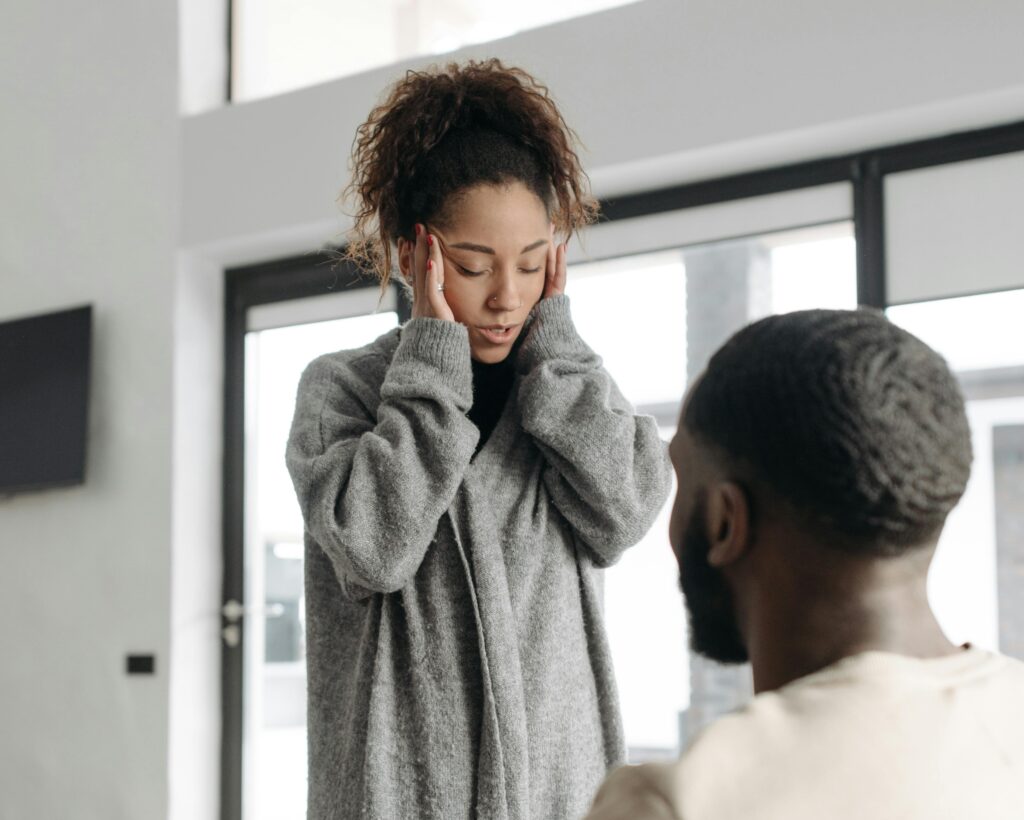 woman standing in front of man holding her head upset