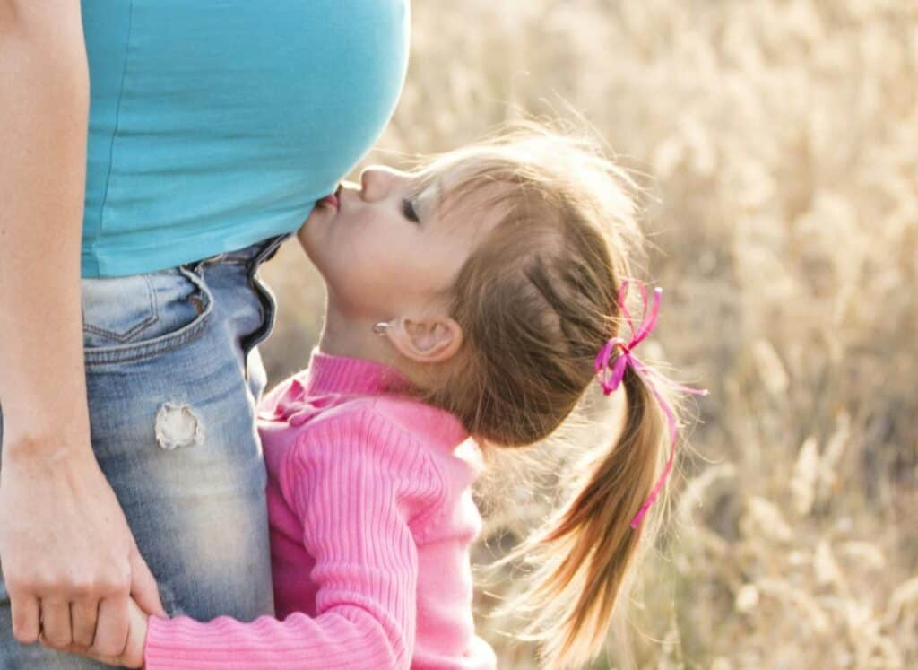 toddler girl kissing mom's pregnant belly