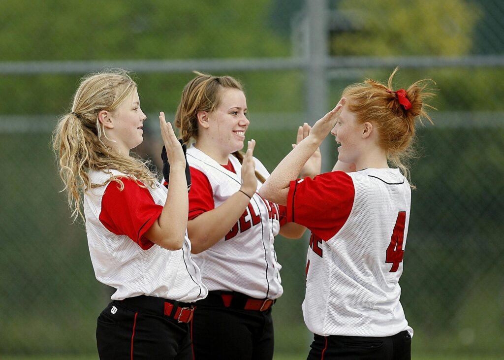 three girls in baseball jerseys high five